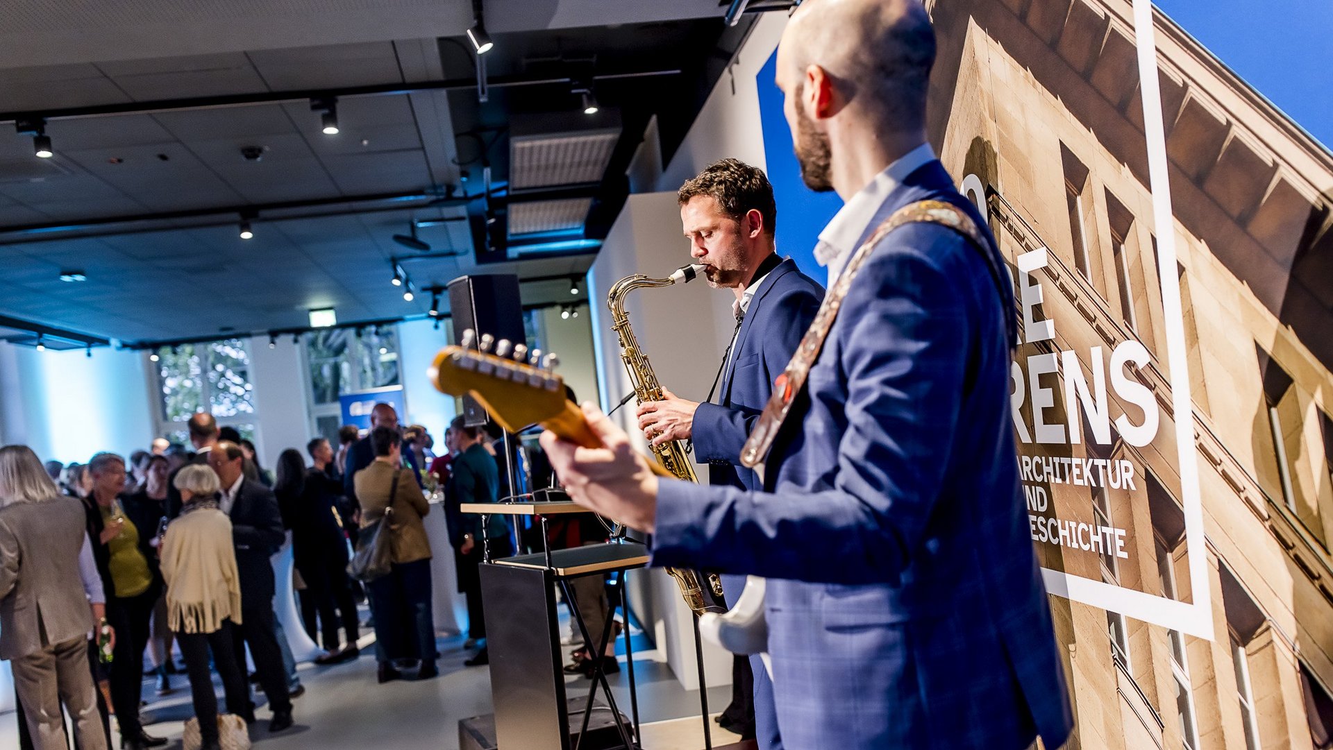 Ein Saxophonist und ein Gitarrist spielen vor Publikum im Behrensbau in Düsseldorf.